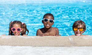 three kids smiling at edge of pool