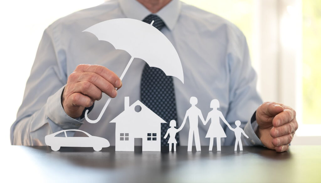 insurance agent holding paper cutover umbrella over paper cut out family, home, and vehicle