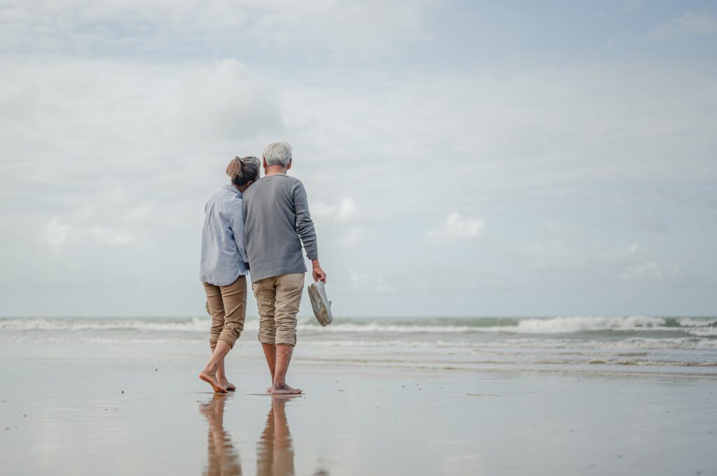 A senior couple walking hand-in-hand on a beach, symbolizing the security and peace of mind life insurance provides in retirement.