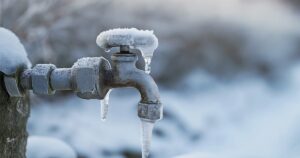 An outdoor residential water spout with icicles dripping in a snowy background, highlighting the need for winterizing faucets to prevent freezing damage.