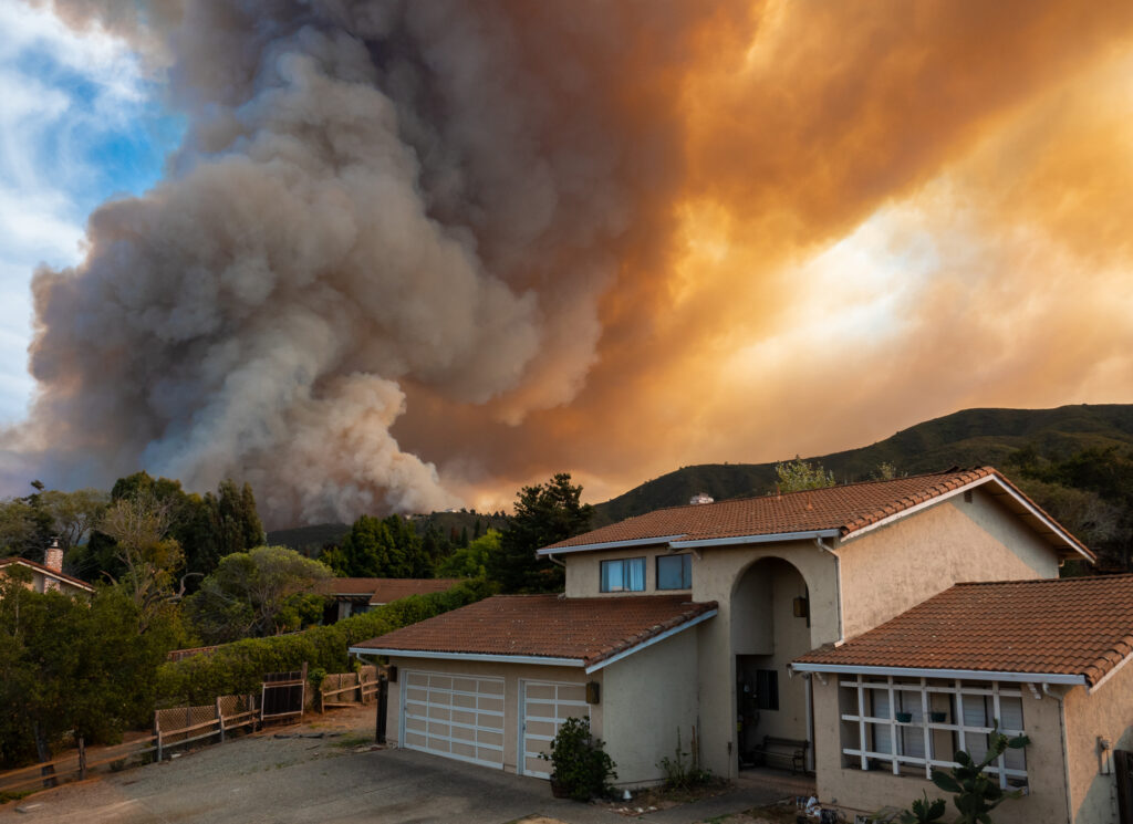 California home with wildfires rolling over the hillside at sunset, highlighting the devastation caused by wildfires.