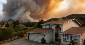 California home with wildfires rolling over the hillside at sunset, highlighting the devastation caused by wildfires.