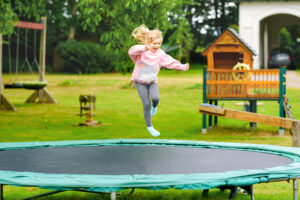 Young child jumping on trampoline outdoors in summer — a potential liability risk for homeowners.