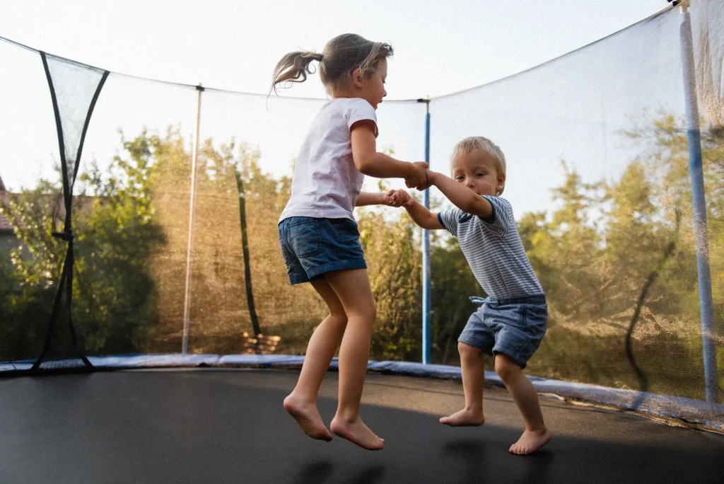 Two children bouncing on a backyard trampoline, highlighting summer recreation and potential liability insurance risks for homeowners.
